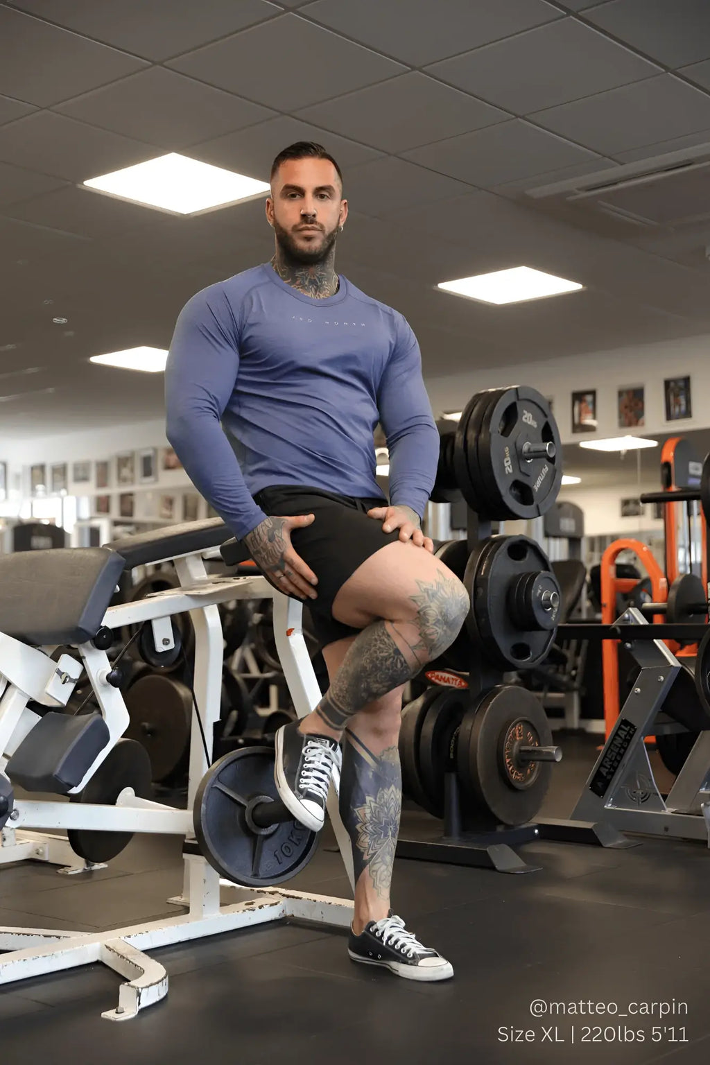 A man with extensive tattoos wearing a fitted steel blue Jed North Agile long sleeve athletic training tee in gym