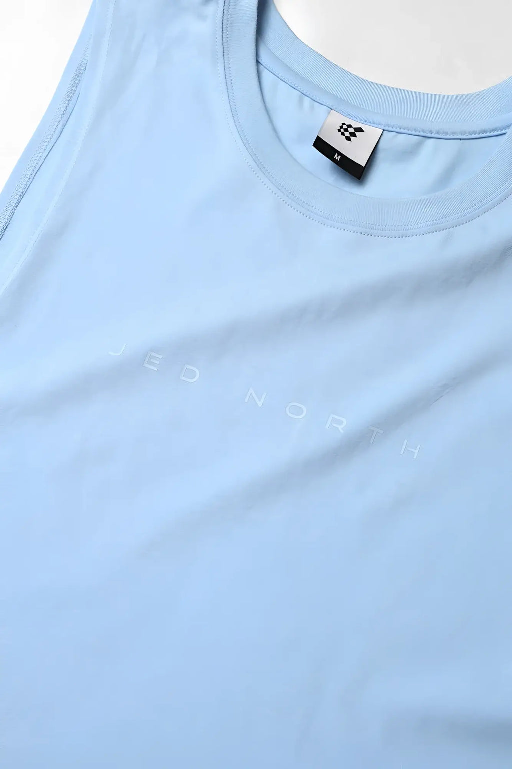 Apollo men’s sleeveless training tee in light blue with subtle jed north lettering and small brand tag at the neckline