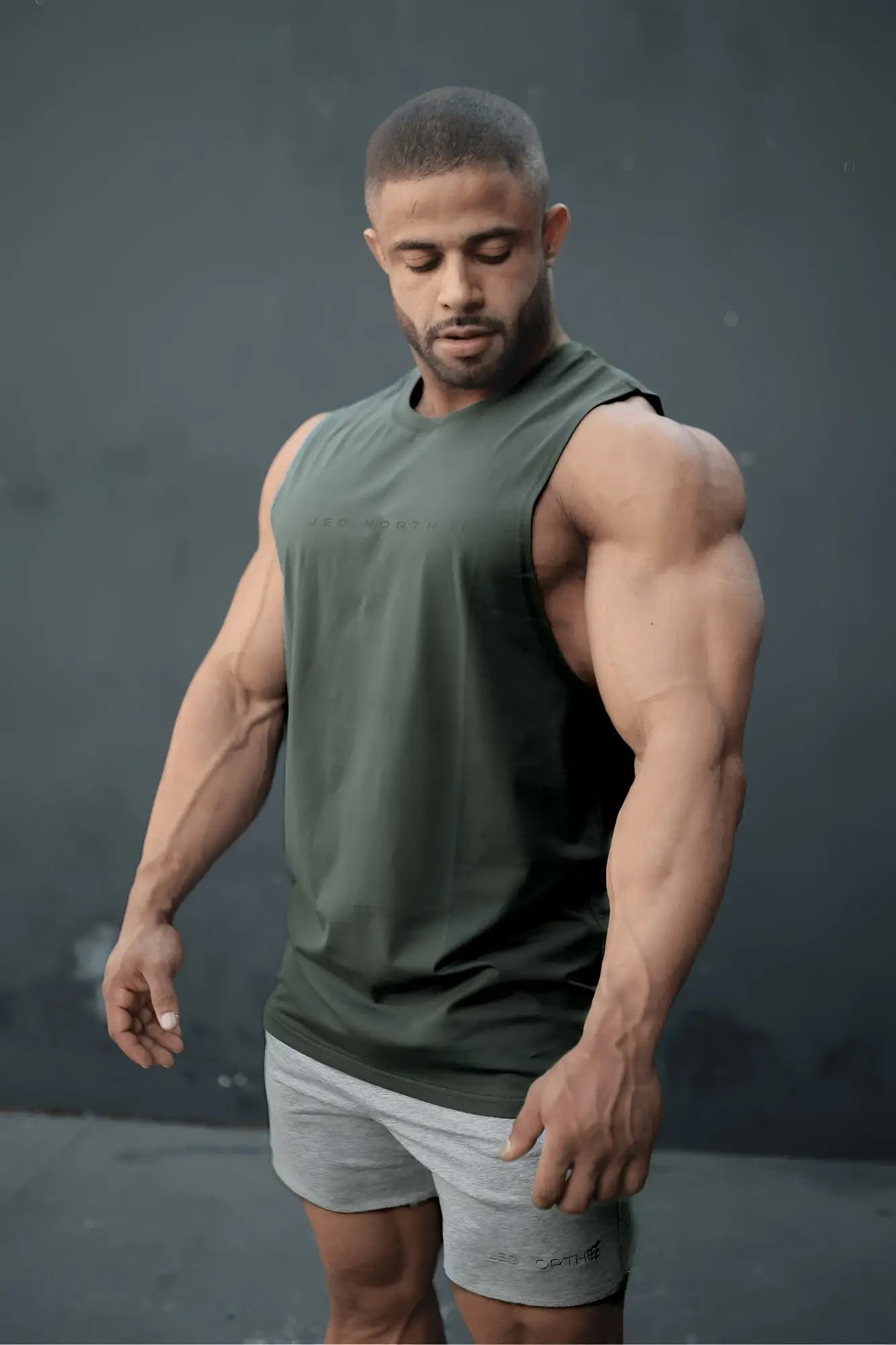 A muscular man wearing an Apollo men’s sleeveless training tee in moss green designed for athletic use