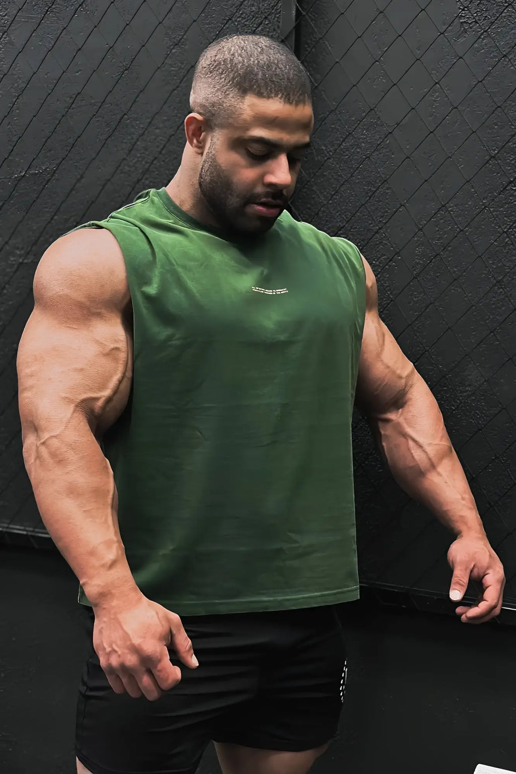 A man wearing a forest green box cut muscle tee with a small white logo on the chest in breathable athletic fabric