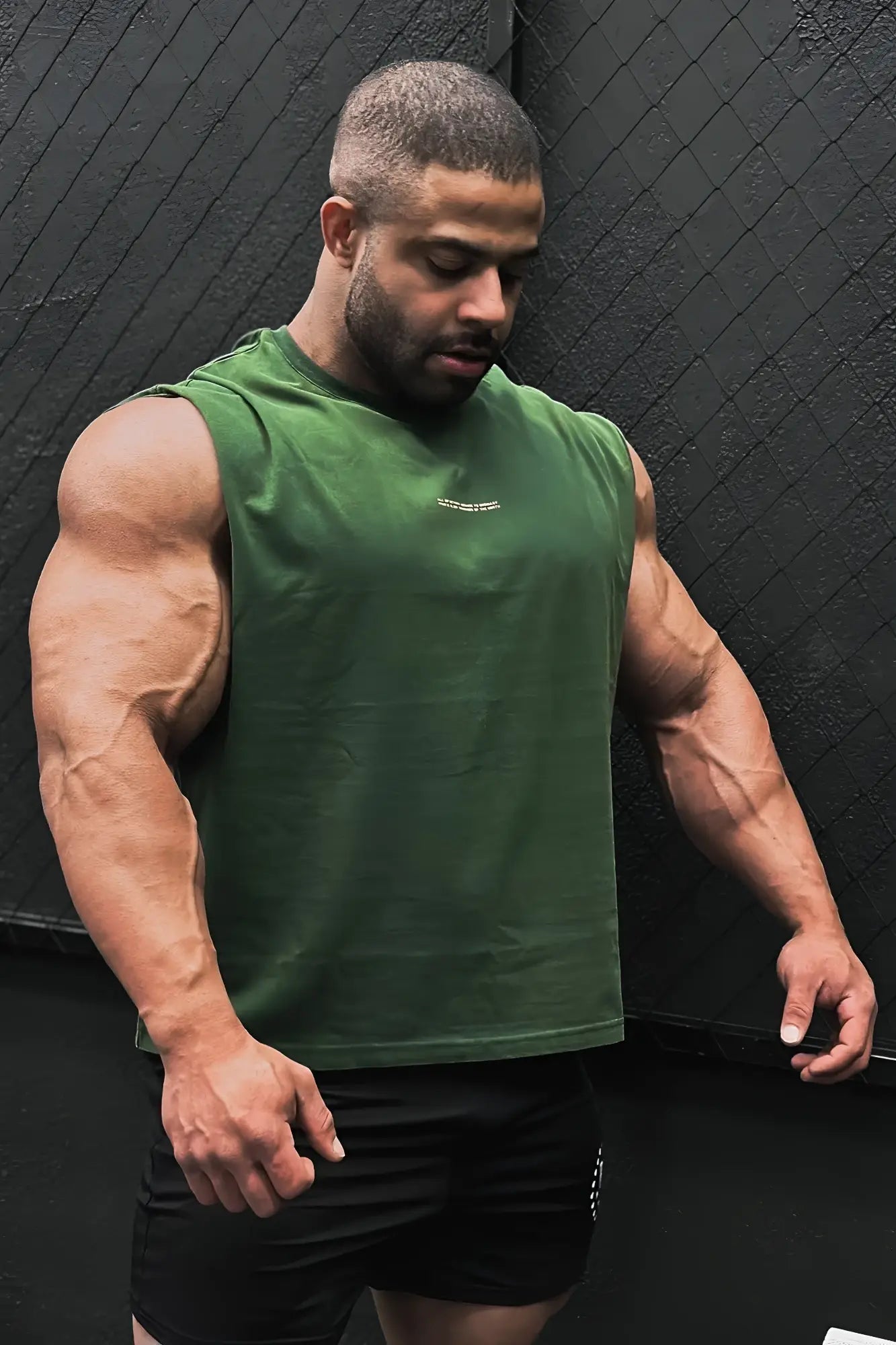 A man wearing a forest green box cut muscle tee with a small white logo on the chest in breathable athletic fabric