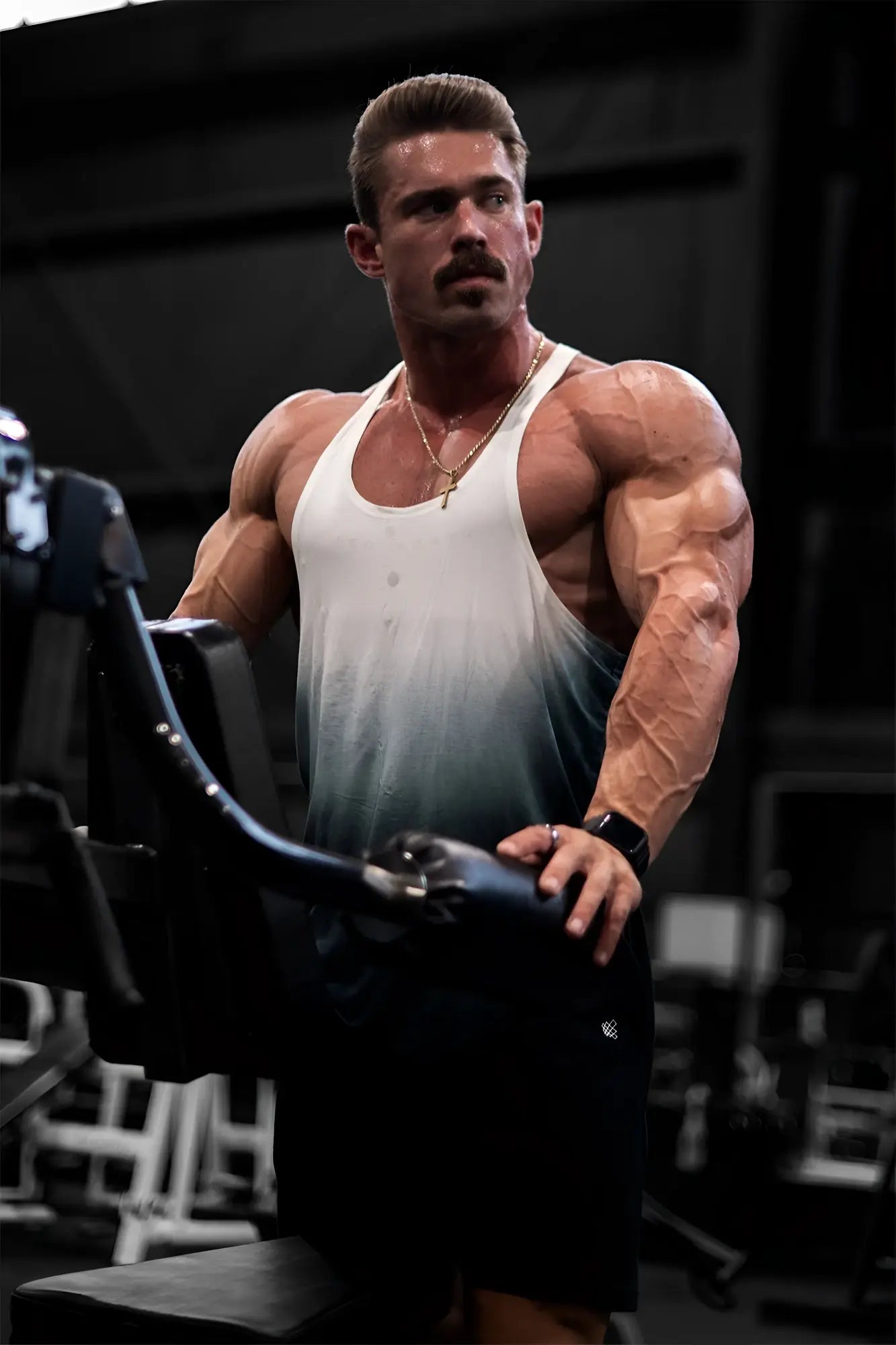 A muscular man wearing a black ombre classic bodybuilding racerback stringer tank top while exercising in a gym