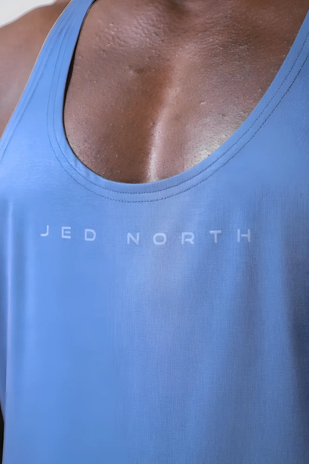 A light blue fitted tank top with a subtle jed north logo designed for classic bodybuilding and racerback stringer style