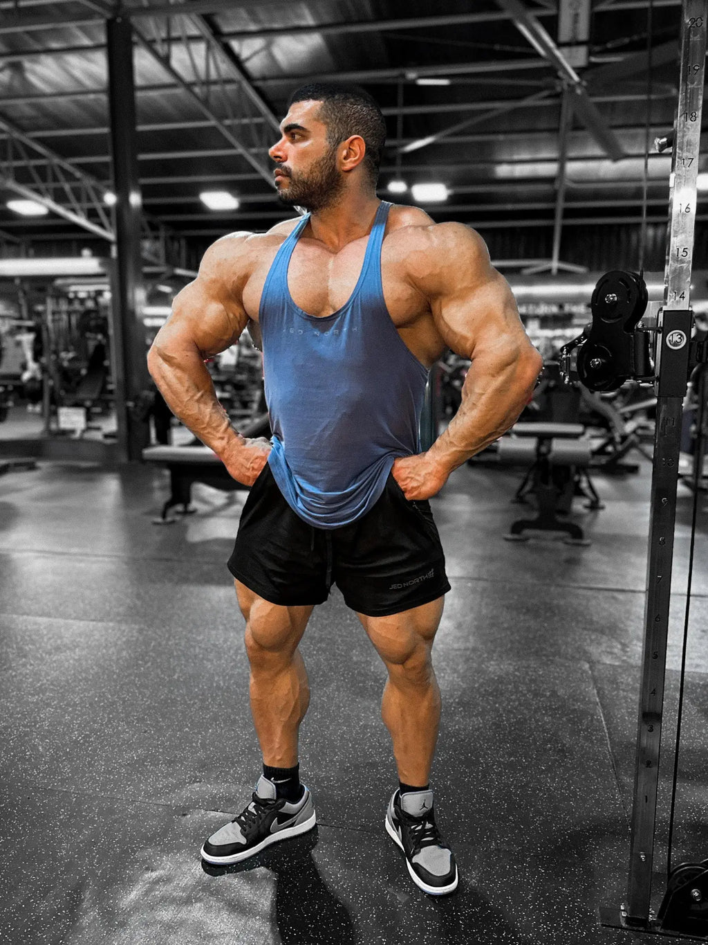 A muscular man wearing a blue Jed North classic bodybuilding racerback stringer tank top in a gym