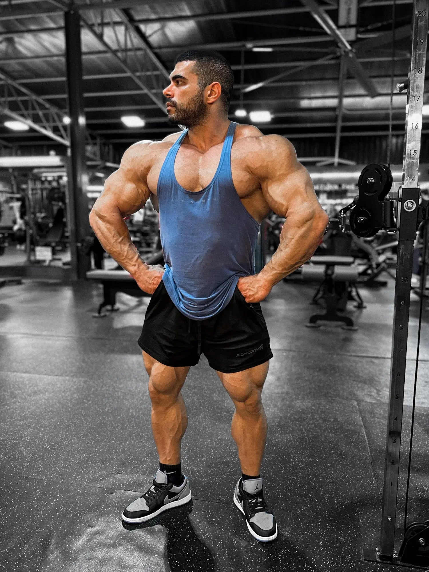A muscular man wearing a blue Jed North classic bodybuilding racerback stringer tank top in a gym