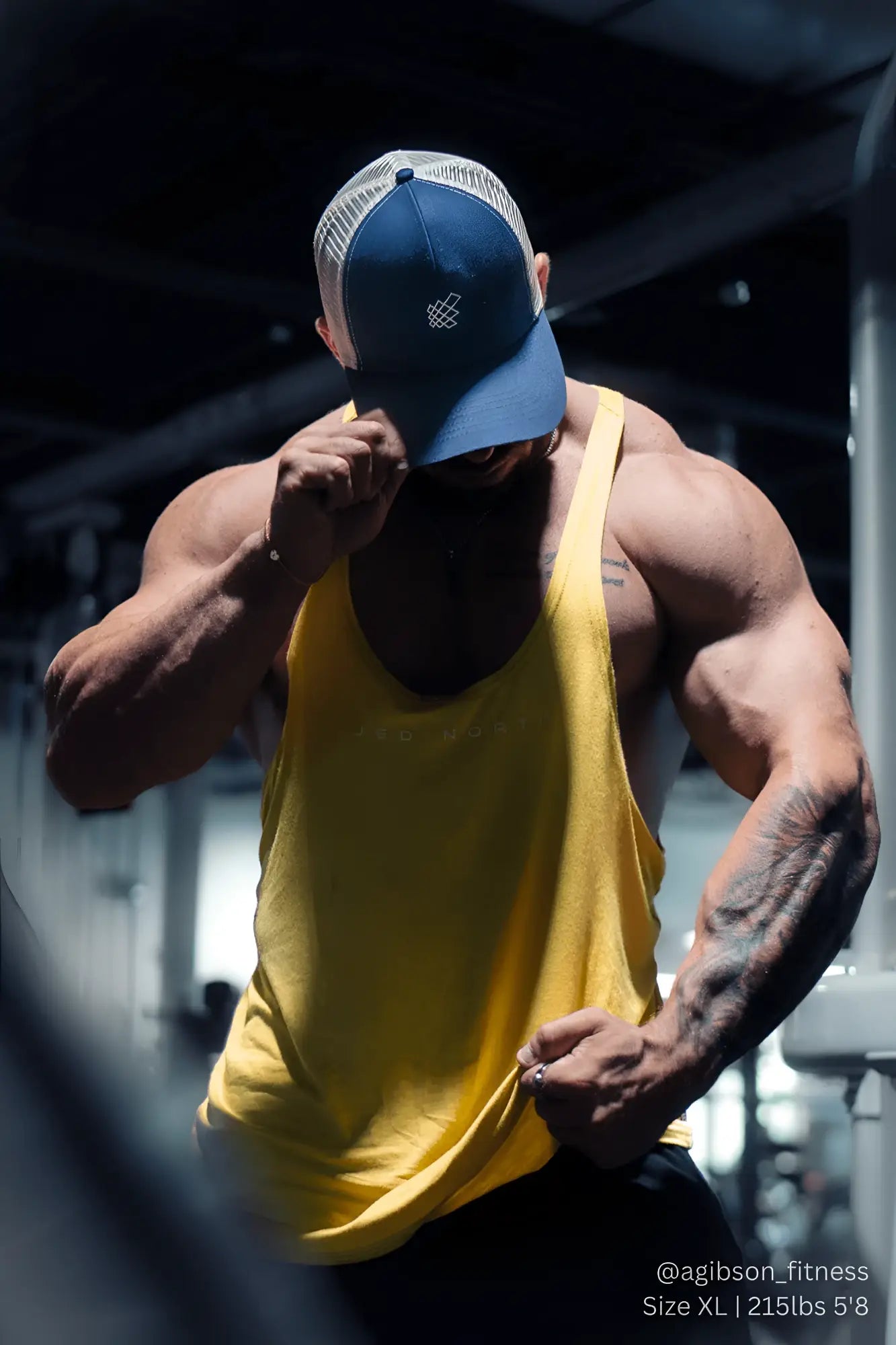 Blue and white trucker hat with a small embroidered logo on the front paired with mustard yellow Jed North Classic Bodybuilding Racerback Stringer