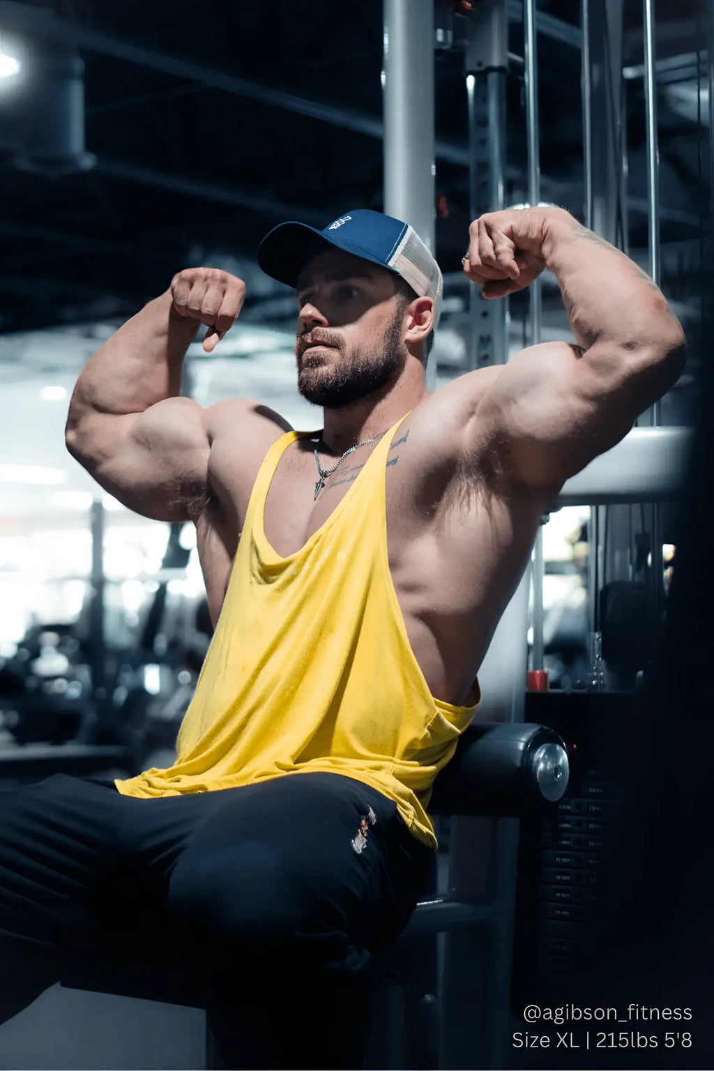 A muscular man wearing a mustard yellow Jed North classic bodybuilding racerback stringer flexing in a gym