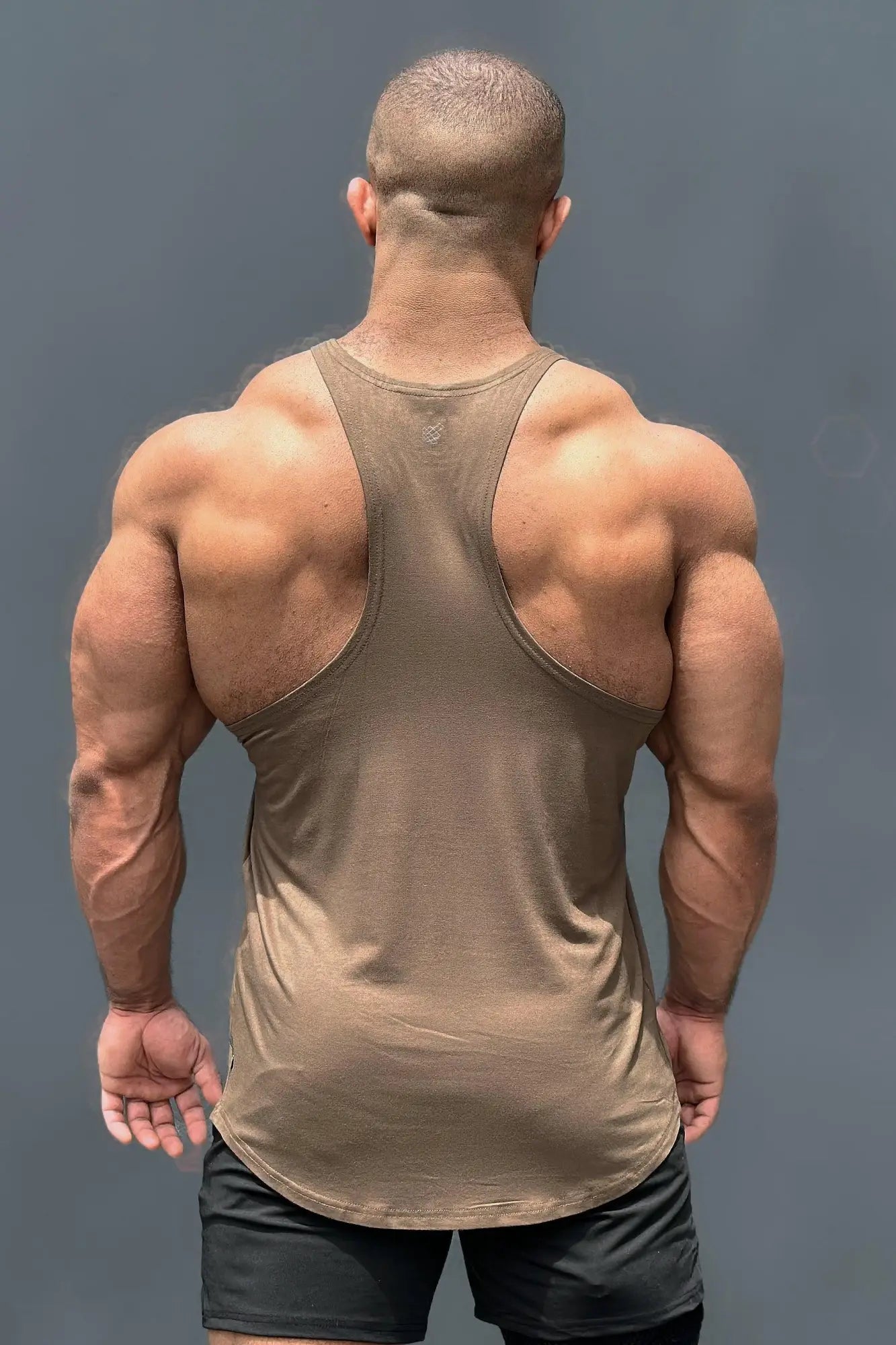 A muscular man wearing a tan sleeveless tank top with racerback design for bodybuilding workouts