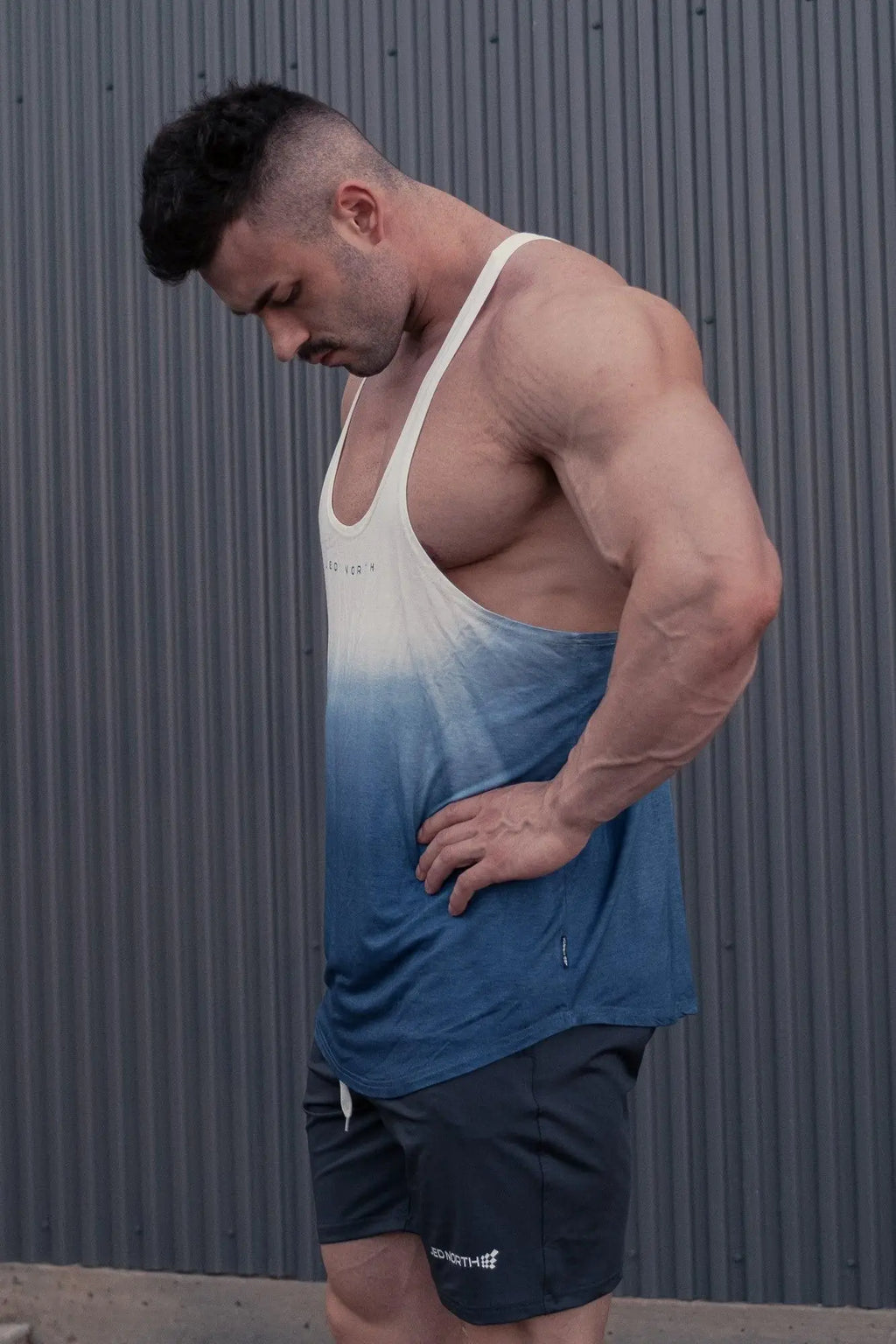 A muscular man wearing a classic bodybuilding racerback stringer tank top in ombre blue and white with black shorts