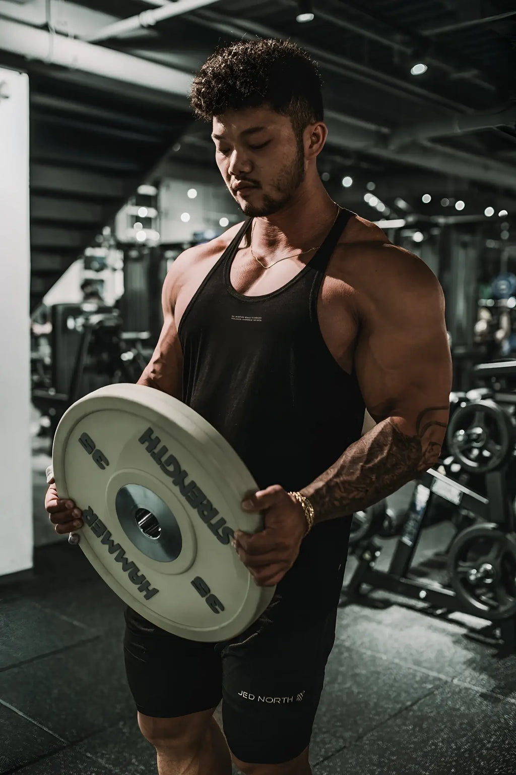 White hummer weight plate with black lettering and central hole next to classic bodybuilding racerback stringer black