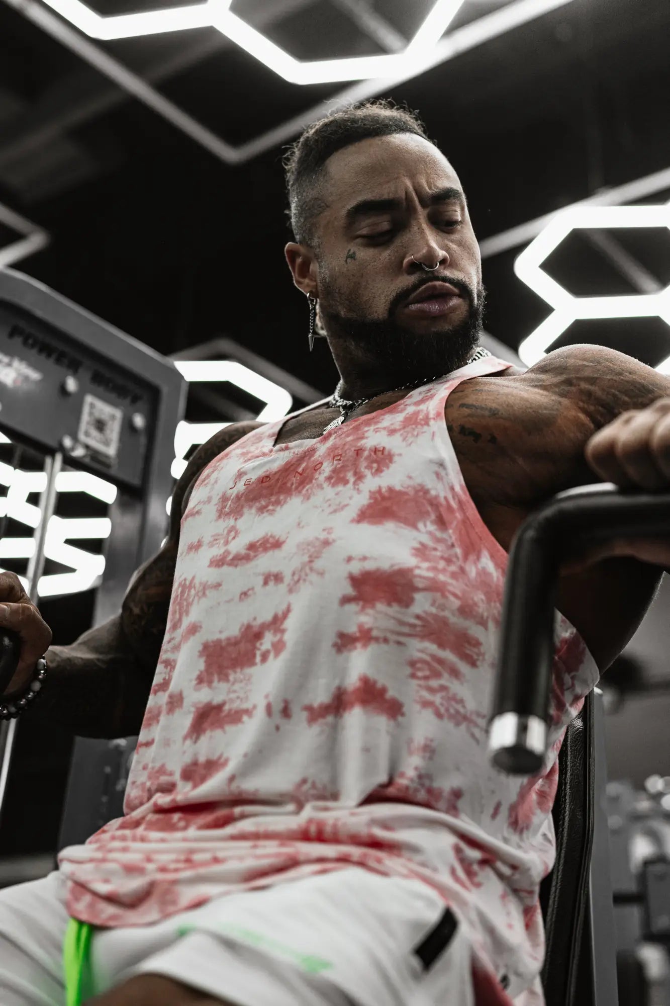 The man is wearing a classic bodybuilding racerback stringer tank top in red white tie dye for gym workouts