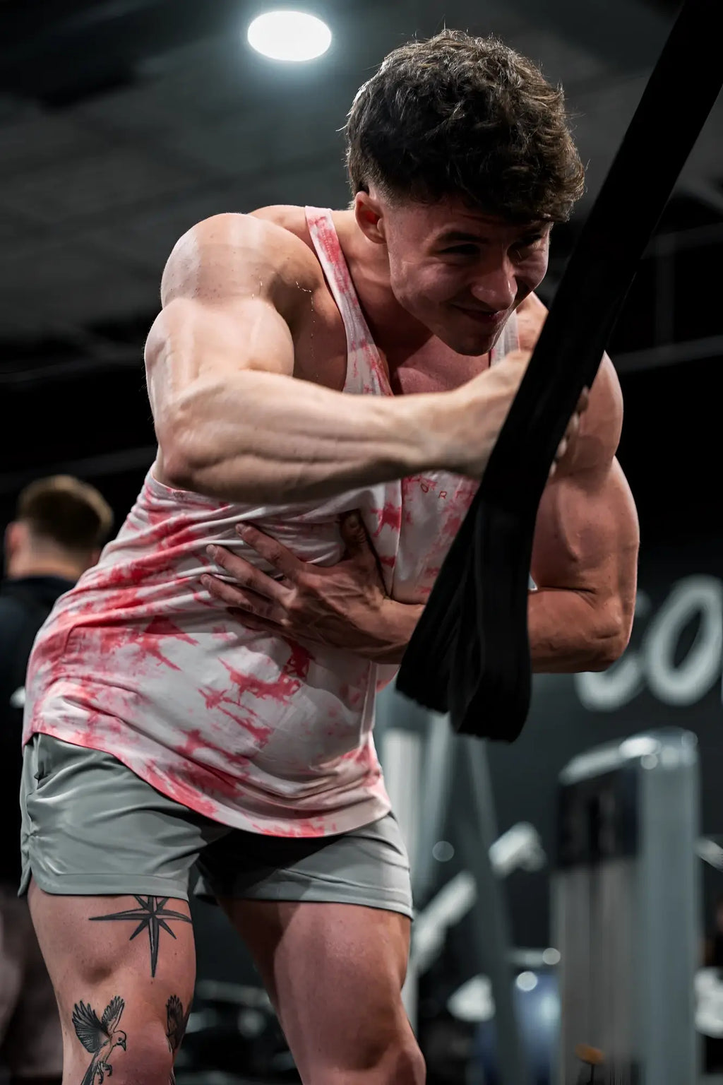 A man wearing a classic bodybuilding racerback stringer tank top in red tie dye with gray shorts from the back side