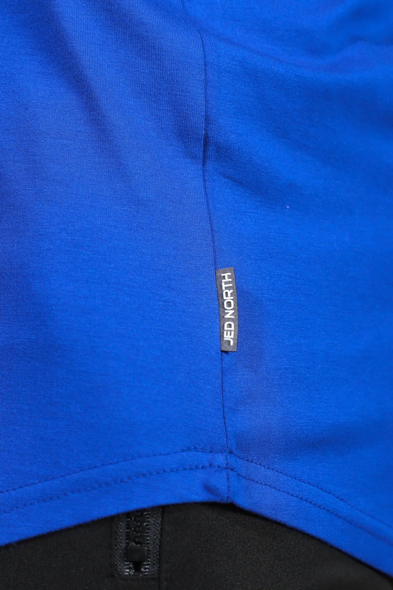 Bright blue classic bodybuilding racerback stringer with black jed north brand tag stitched near the seam