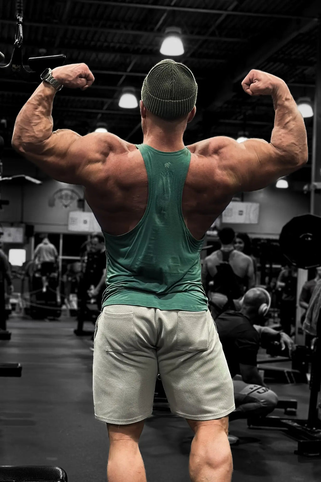 A muscular man flexing back muscles wearing the back of a sea green classic bodybuilding racerback stringer in gym