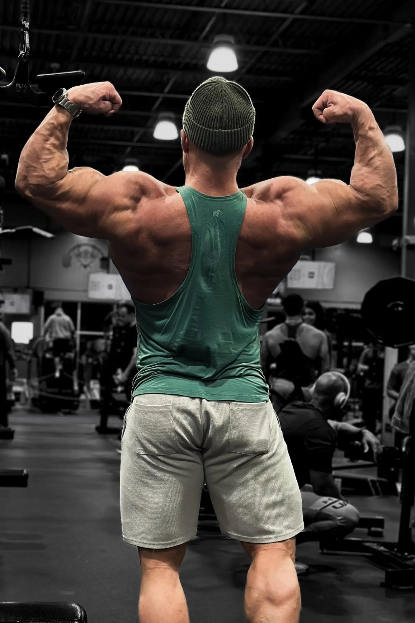 A muscular man flexing back muscles wearing the back of a sea green classic bodybuilding racerback stringer in gym