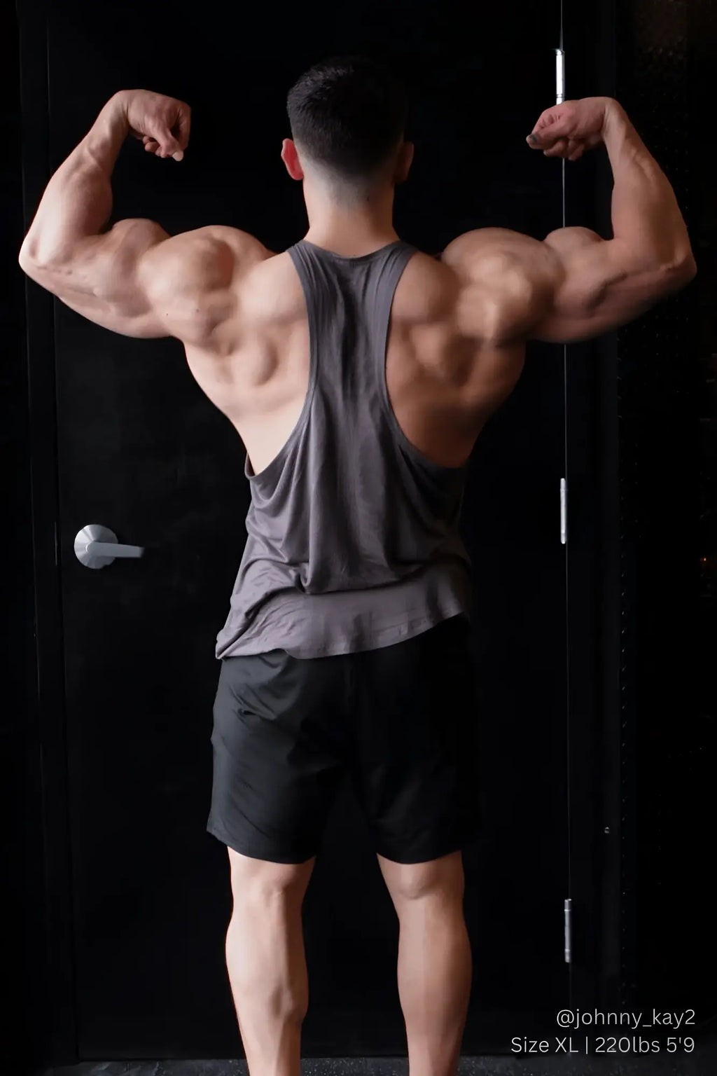 A muscular man flexing back muscles wearing jed north classic bodybuilding racerback stringer in steel gray back view