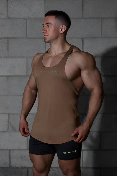 Tan sleeveless Jed North Classic bodybuilding racerback stringer with light branding paired with black shorts