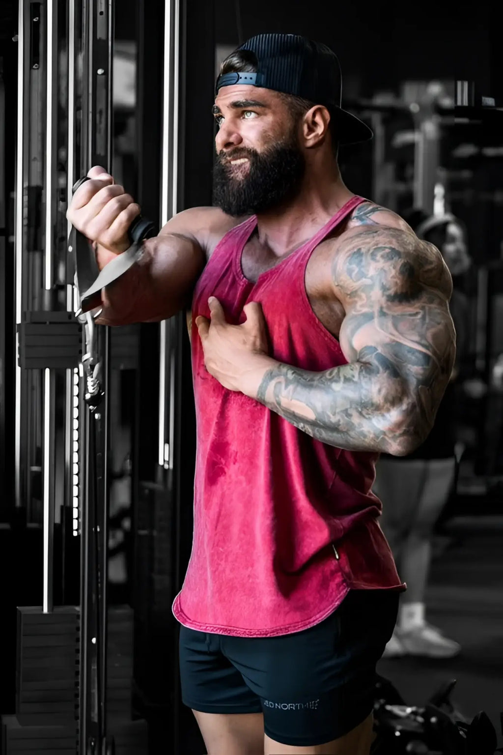 A muscular man with beard and tattoos wears a faded red Jed North classic vintage washed racerback stringer crimson tank top