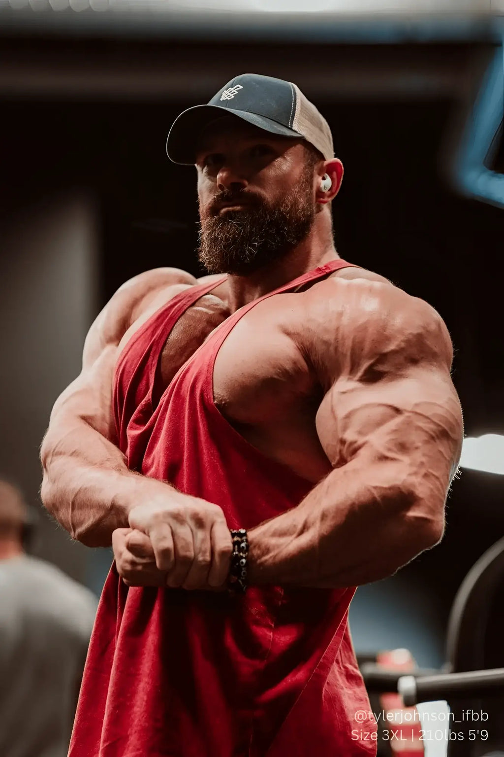 A muscular man wearing a crimson Jed North classic vintage washed racerback stringer and a dark baseball cap