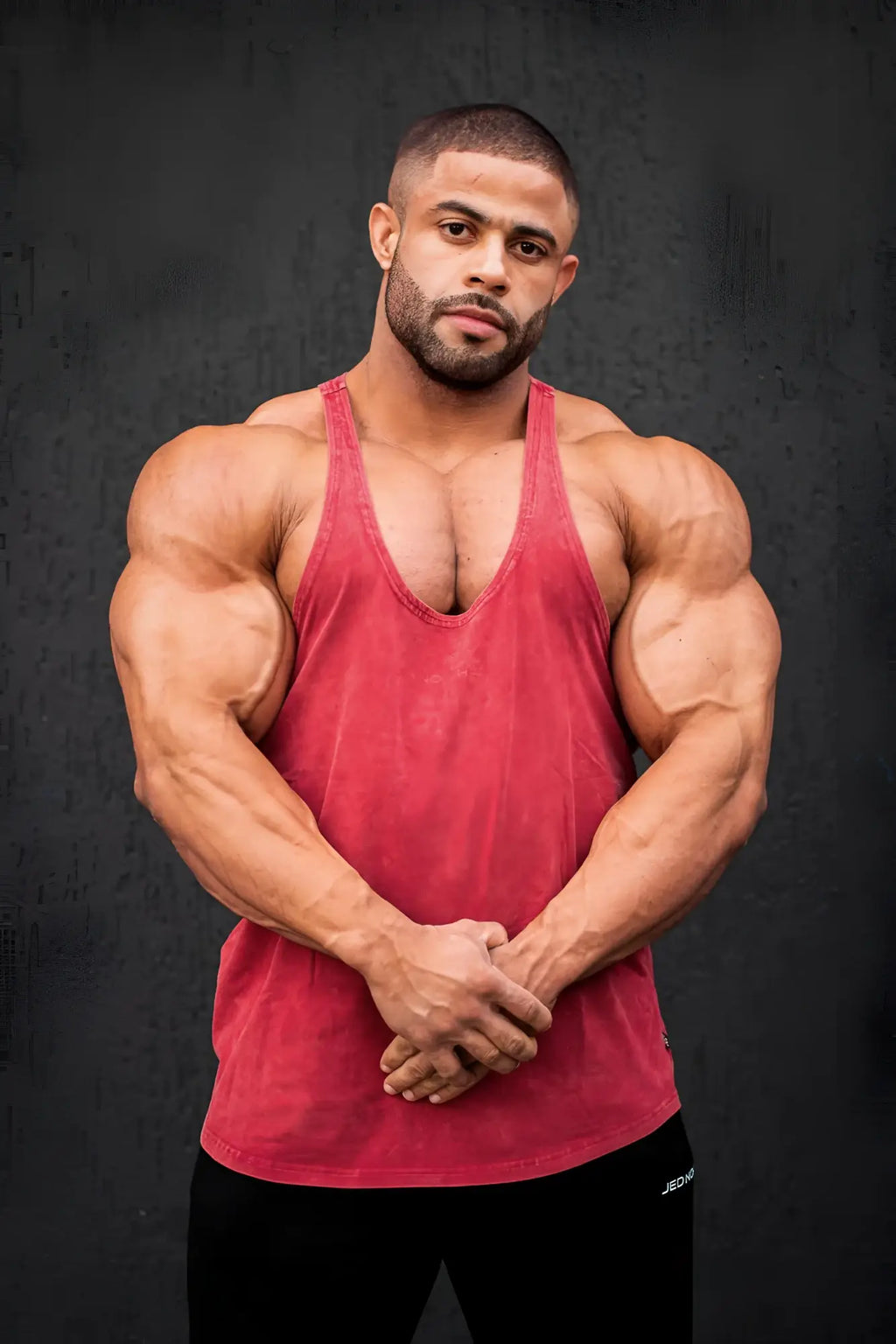 A muscular man wearing a Jed North classic vintage washed racerback stringer tank top in crimson textured fabric