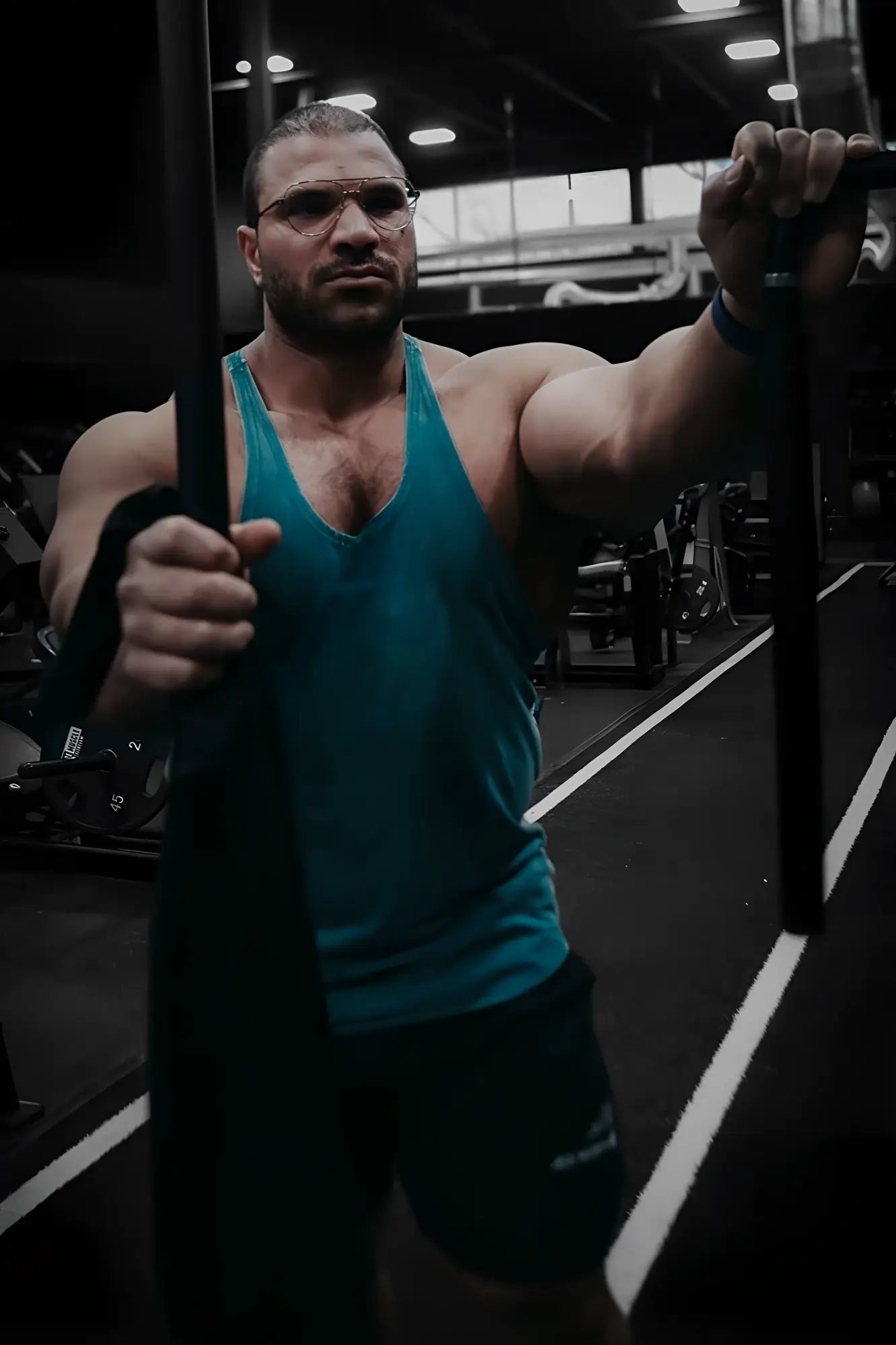 A muscular man wearing a deep sea teal jed north classic vintage washed racerback stringer gripping weights in a gym