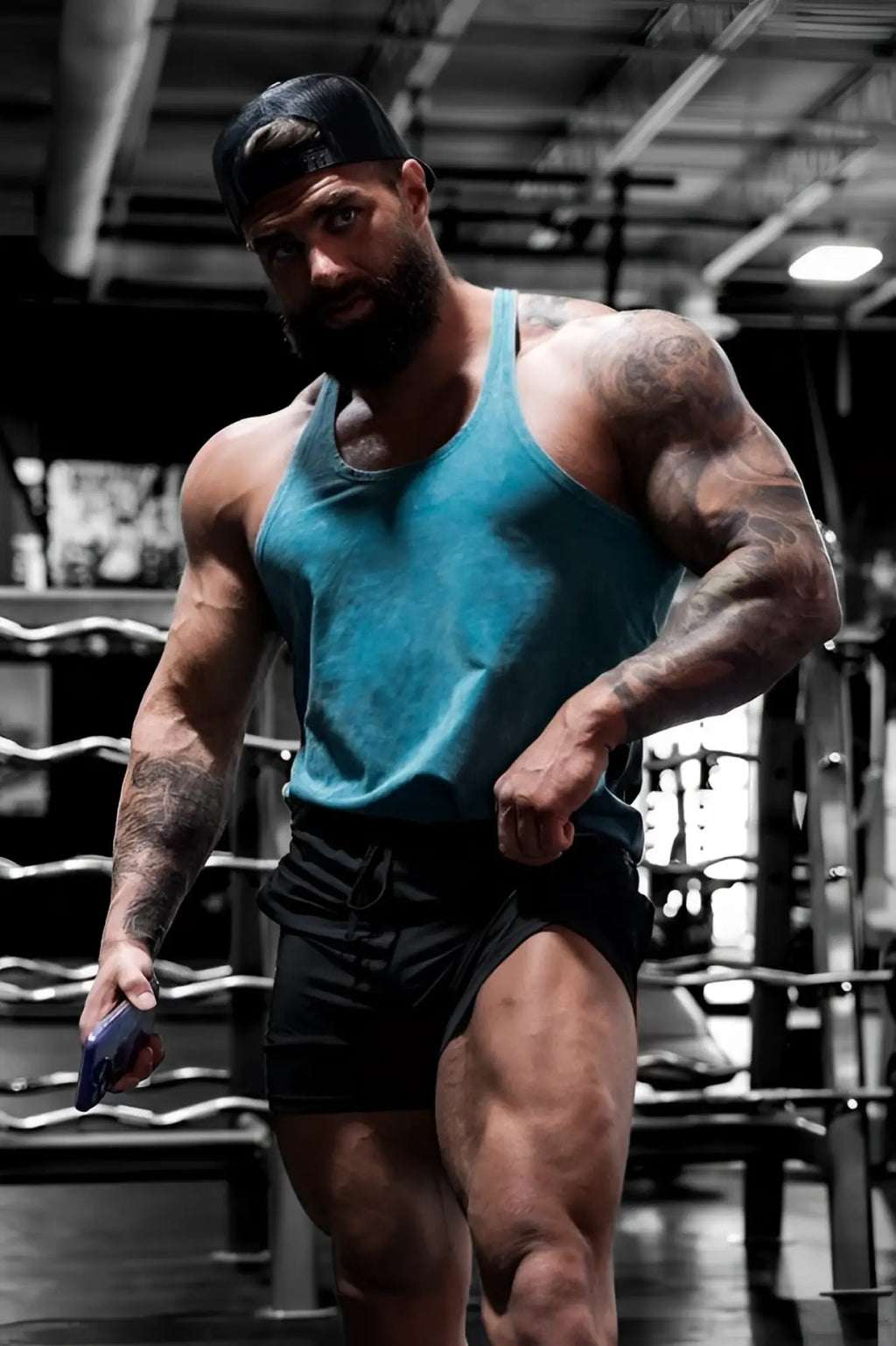 A muscular man wearing a teal Jed North classic vintage washed racerback stringer with black shorts and arm tattoos