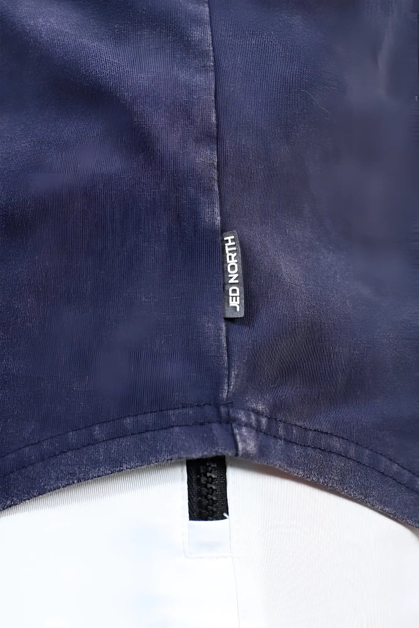Dark blue denim fabric with black jed north brand tag stitched near the hem of jed north classic vintage washed racerback