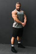 A muscular man wearing a gray cotton training stringer tank top and black shorts for gym workouts