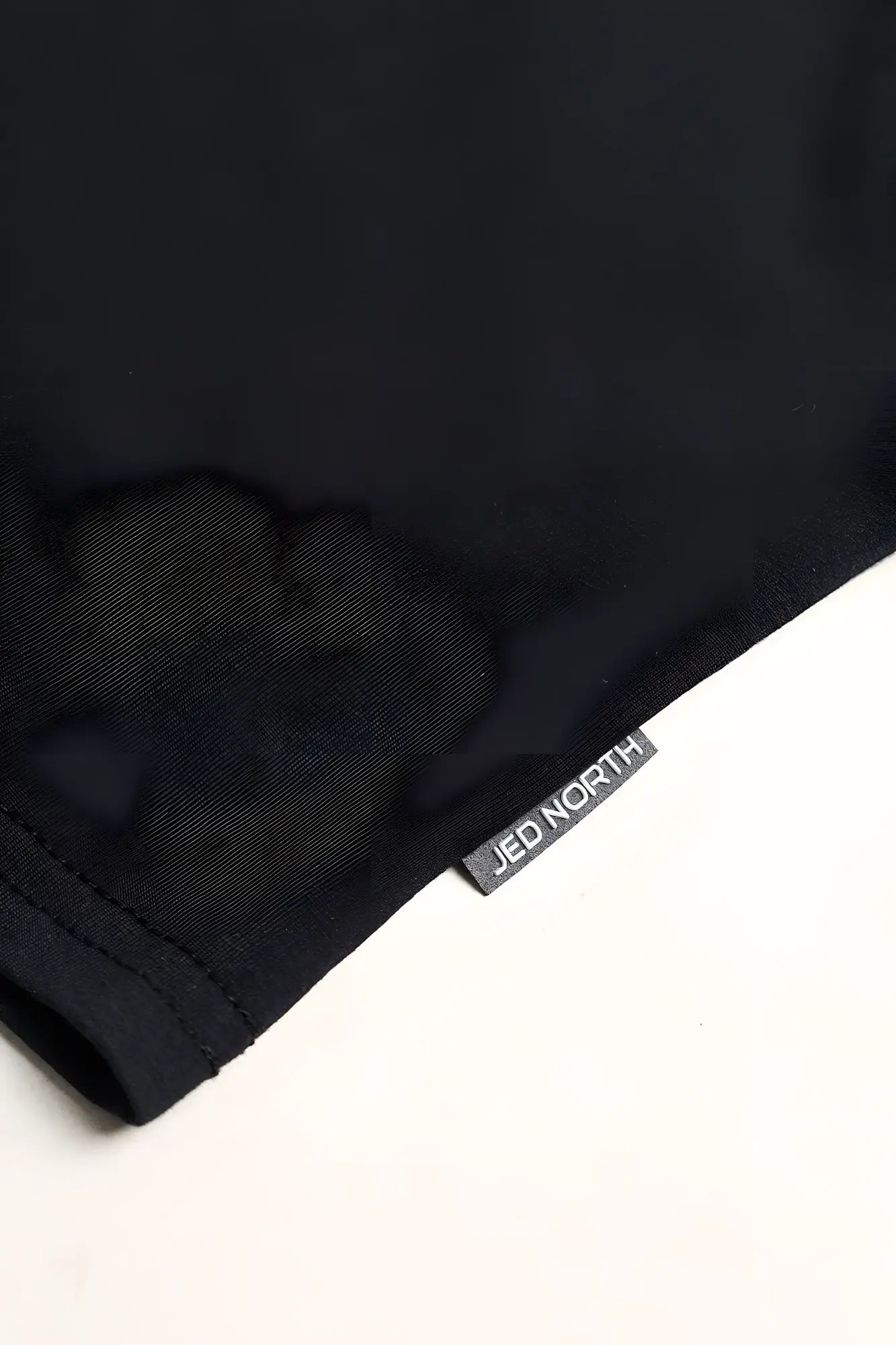 Black cotton training stringer t-shirt with small gray jed north woven label at the hem in midnight color