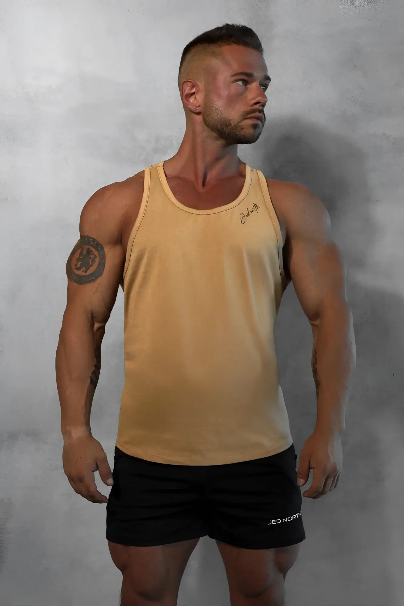A tan cotton training stringer tank top with a subtle signature embroidered on the upper left chest
