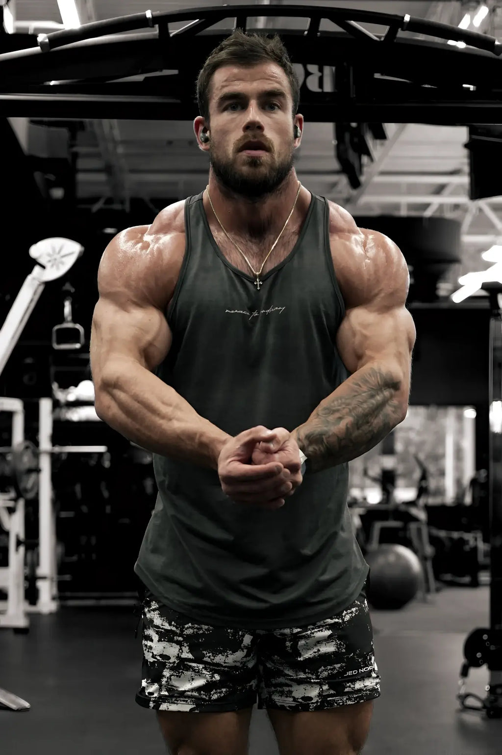A muscular man wearing a dark gray Jed North Dynamic bodybuilding stringer tank top for gym workouts