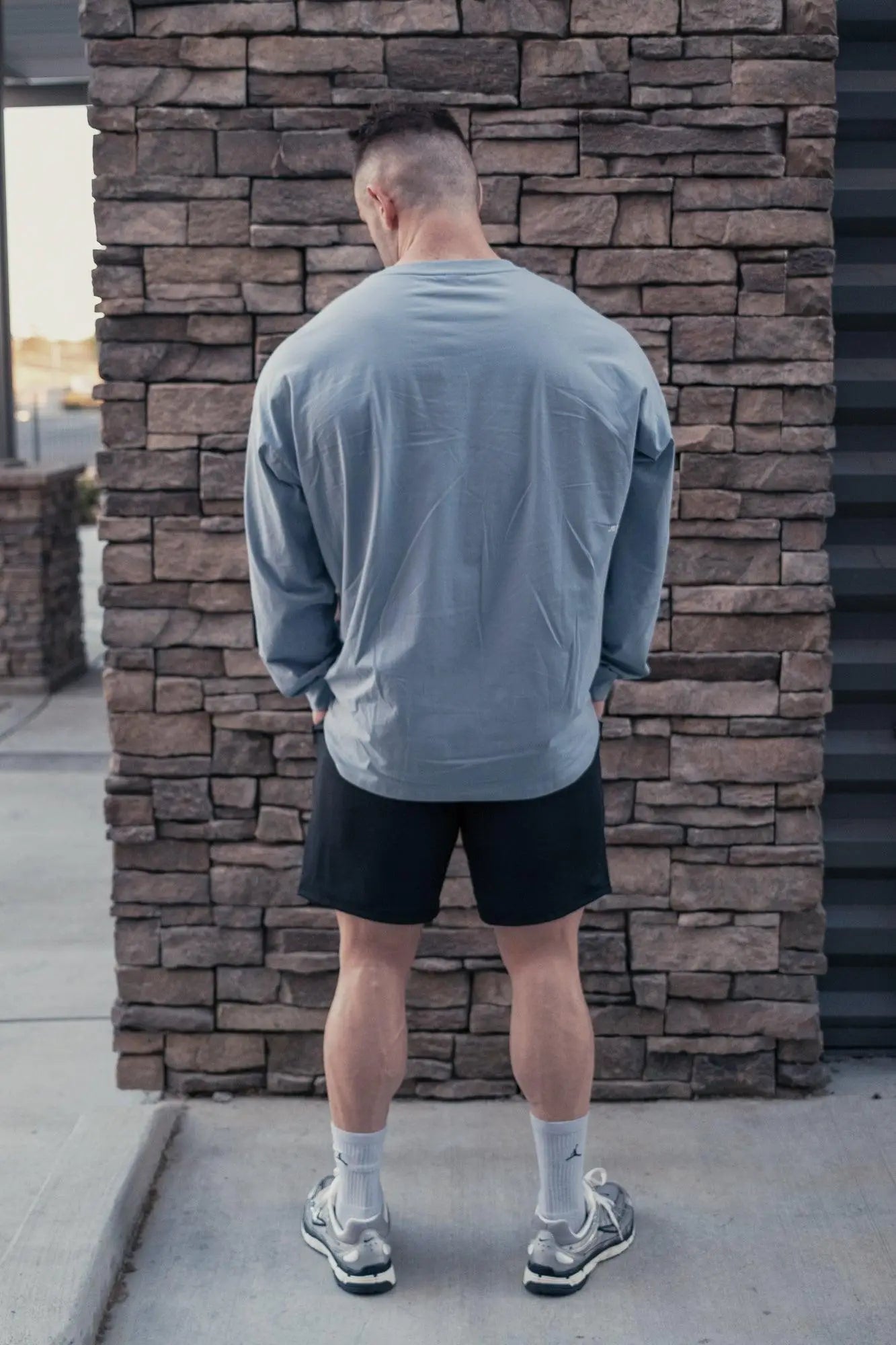 A man wearing the back of a Jed North Energy oversized long sleeve t shirt 2.0 in arctic blue stands with black shorts