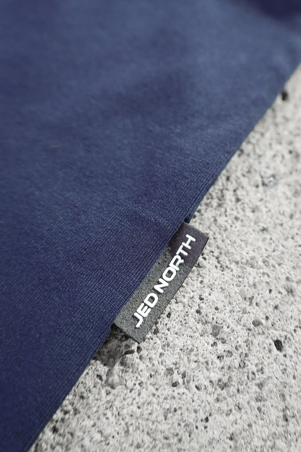 Dark blue fabric with a black woven label showing white jed north text on the jed north energy oversized long sleeve t shirt 2.0