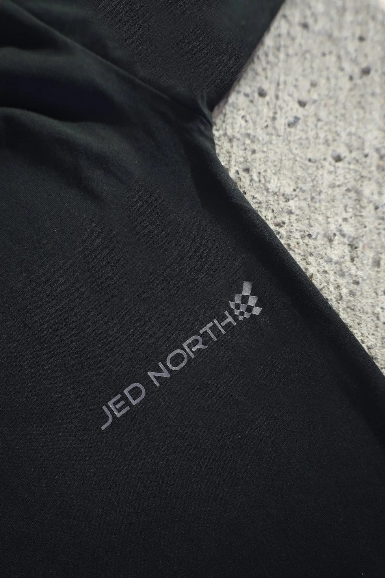 Black fabric of jed north energy oversized long sleeve t-shirt 2.0 obsidian black with gray logo and checkered flag emblem near sleeve