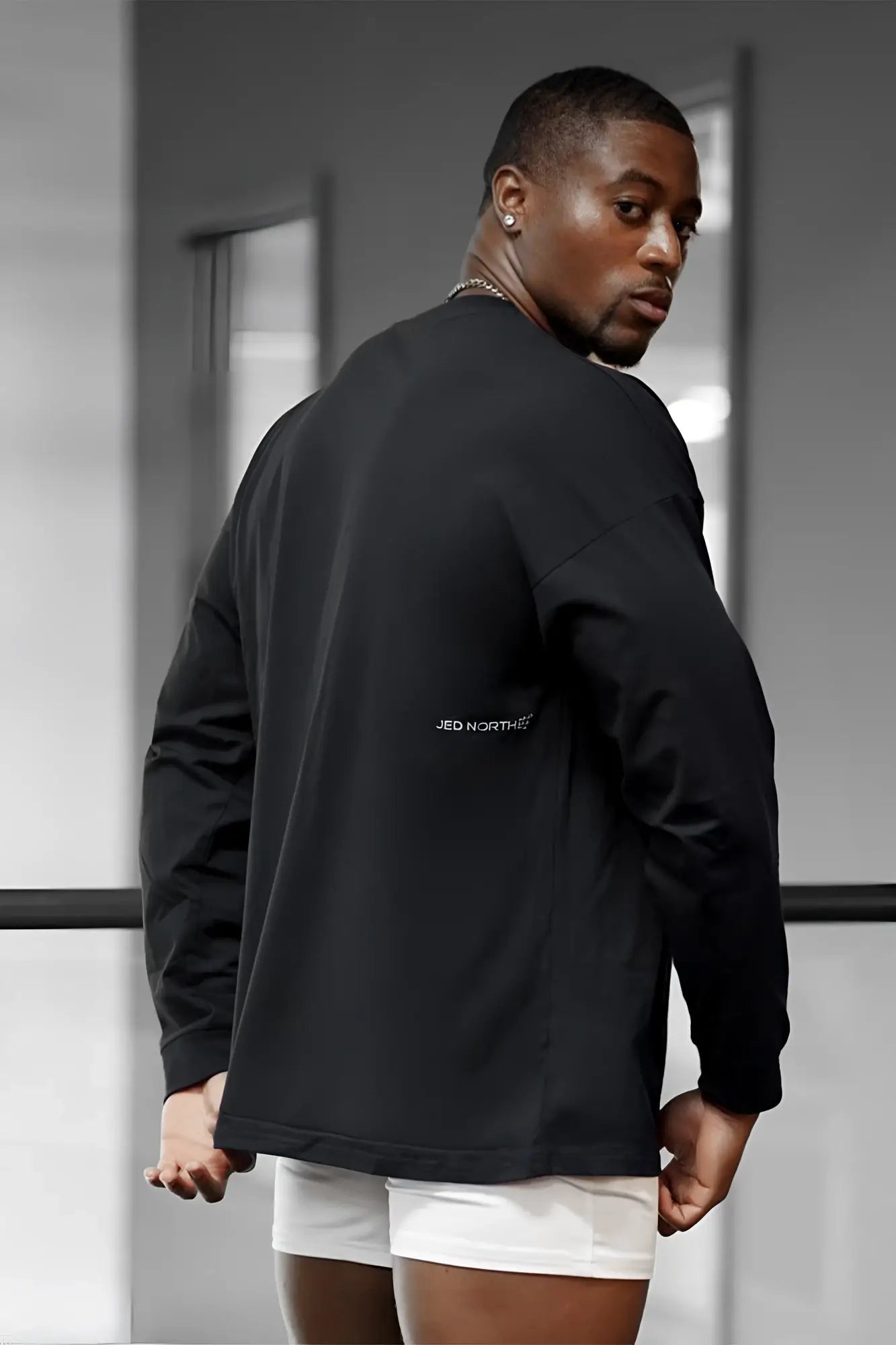 Back view of jed north energy oversized long sleeve t-shirt 2.0 in obsidian black with subtle branding on a black jacket
