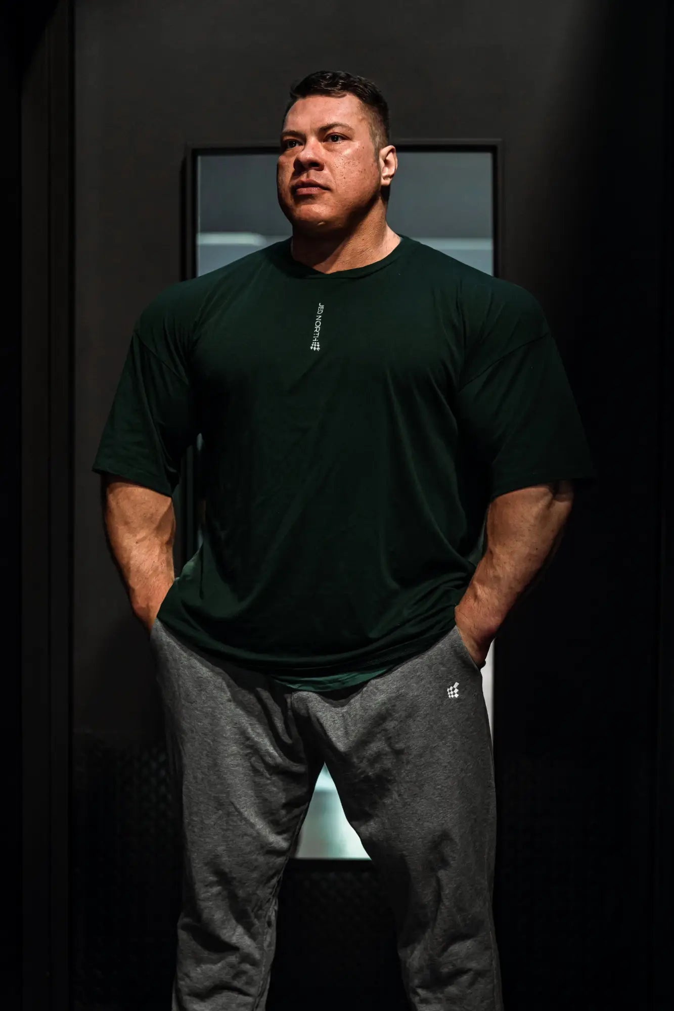 Dark green jed north energy oversized t-shirt with small white logo paired with gray sweatpants and subtle brand emblem