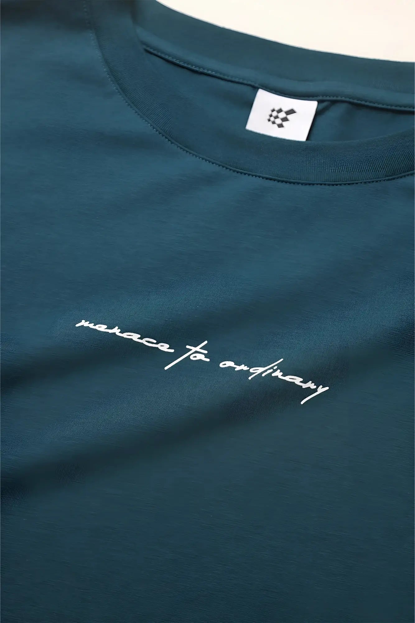 Energy oversized teal cotton t-shirt with white cursive embroidery reading manace to ordinary across the chest