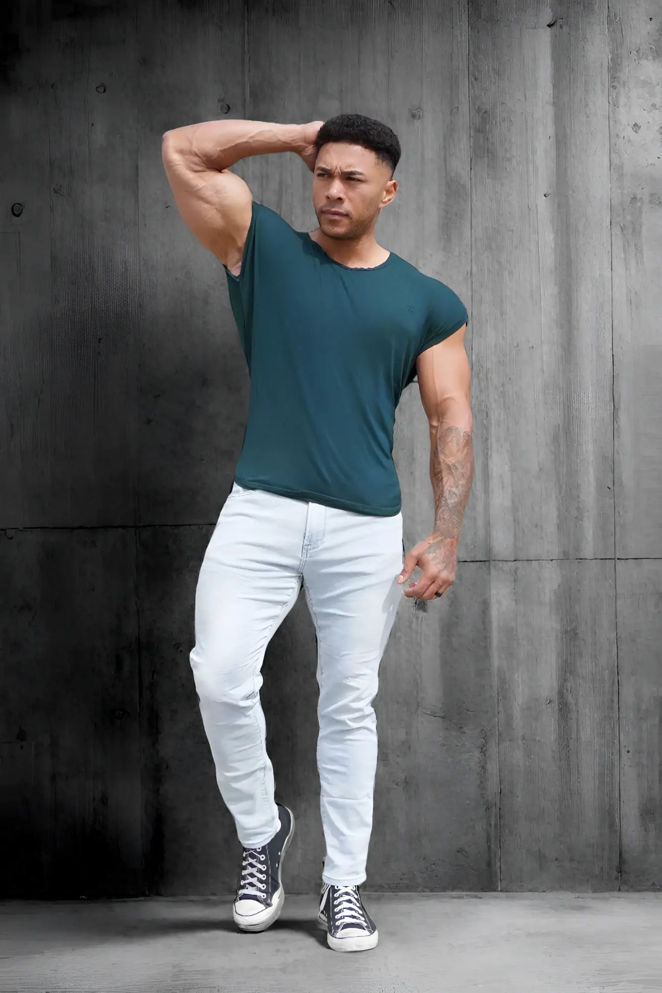 A muscular man wearing a dark teal jed north evolve mens cap sleeve t-shirt 2.0 paired with white jeans