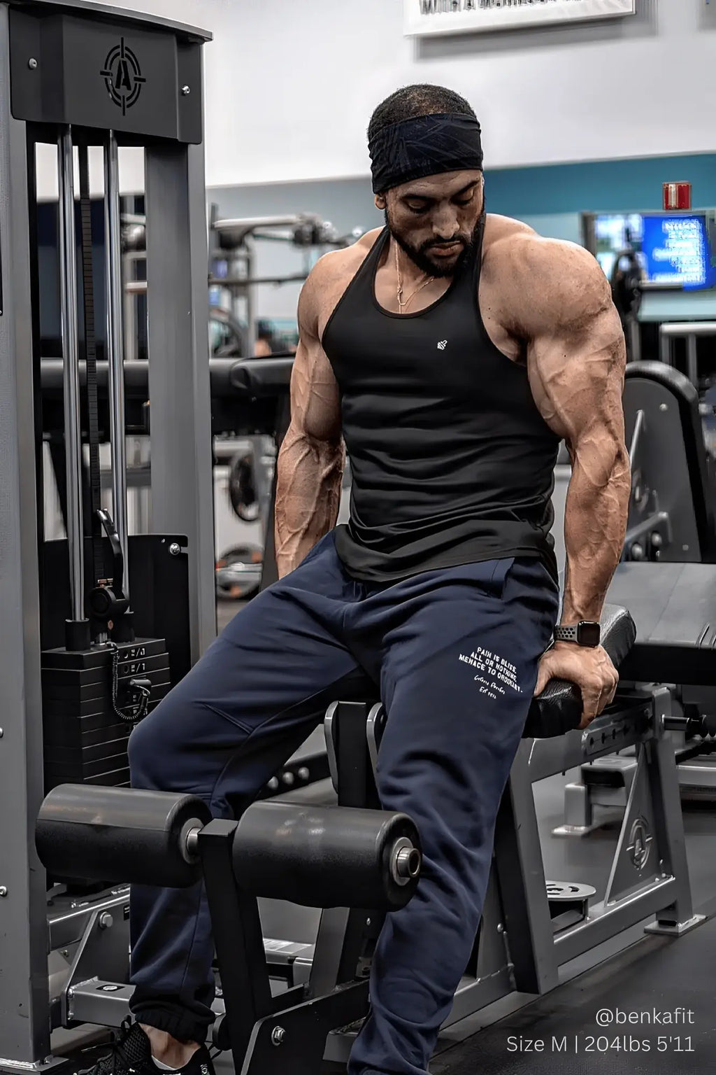 Muscular man seated on gym machine wearing jed north fast-dry bodybuilding workout stringer in black tank top style