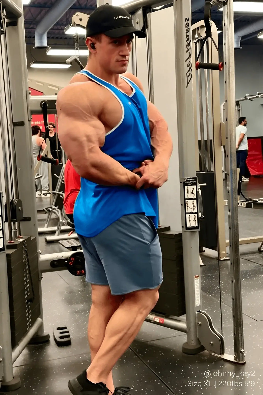A muscular man wearing a jed north fast-dry bodybuilding workout stringer in blue with white trim in a gym