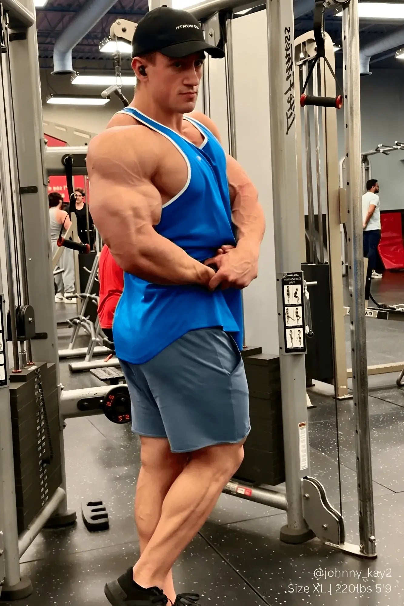 A muscular man wearing a jed north fast-dry bodybuilding workout stringer in blue with white trim in a gym