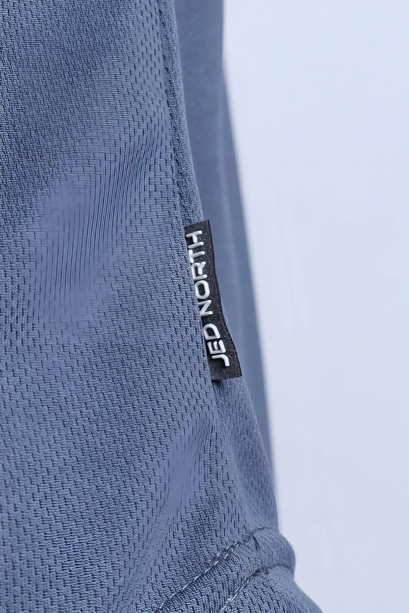A black rectangular jed north label sewn into the seam of a textured blue fast dry bodybuilding workout stringer
