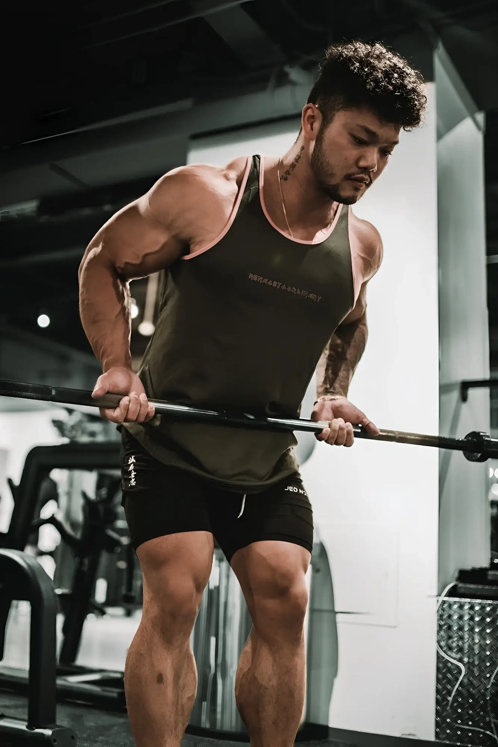 A muscular man performing a barbell row in a fast-dry bodybuilding workout stringer gray with pink trim in the gym