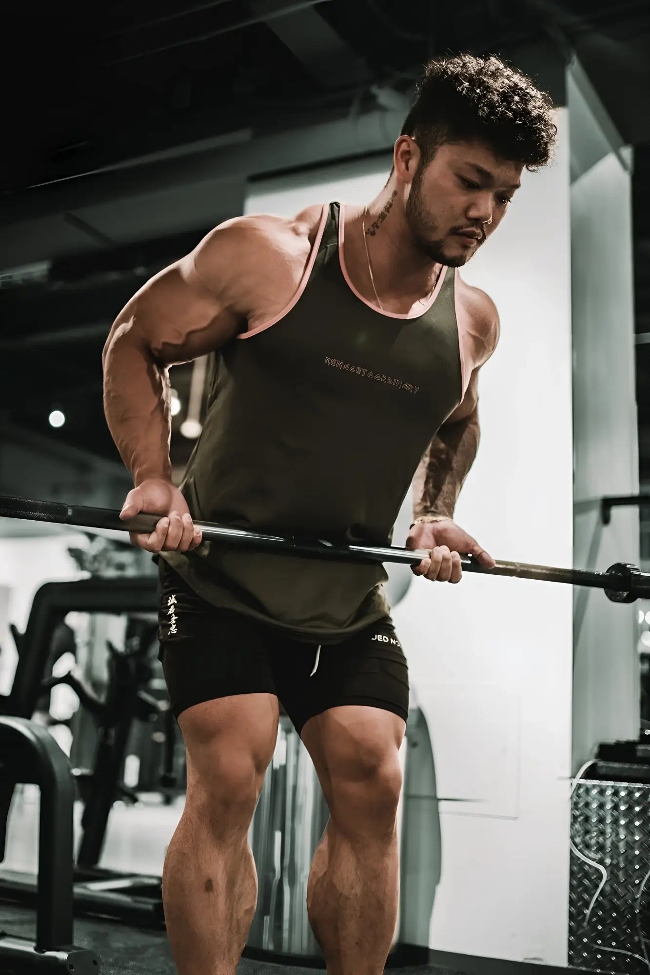 A muscular man performing a barbell row in a fast-dry bodybuilding workout stringer gray with pink trim in the gym