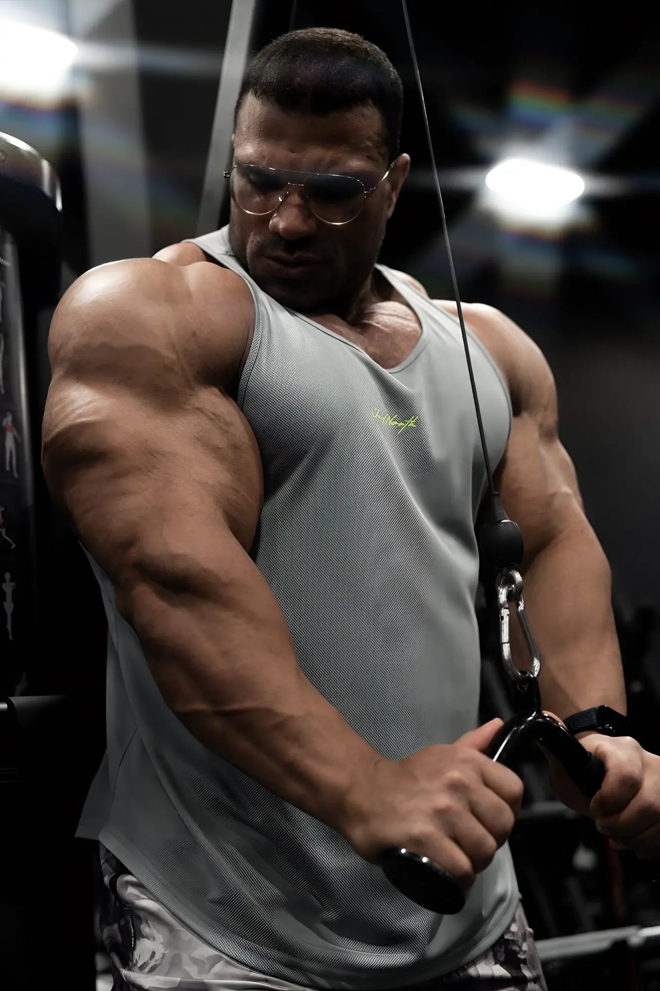 A muscular man performs cable exercises wearing a light gray fast-dry bodybuilding workout stringer with neon logo