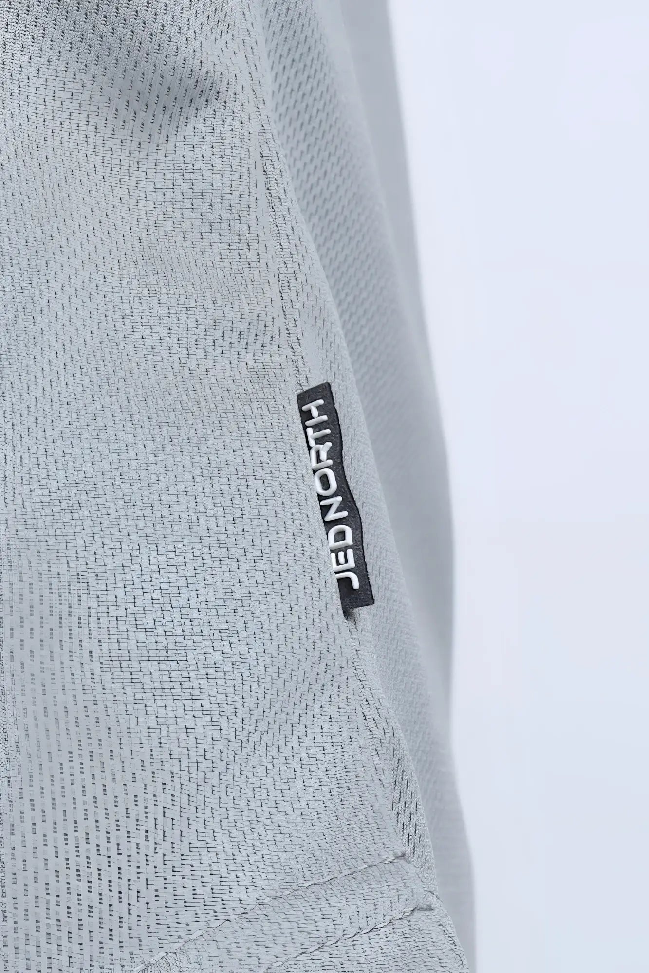 Light gray textured fabric of fast-dry bodybuilding workout stringer with black jed north brand tag stitched in seam