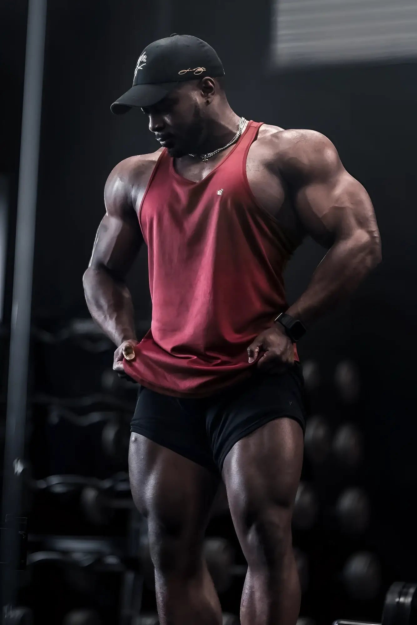 A muscular man wearing a maroon Jed North fast-dry bodybuilding workout stringer tank top and black shorts