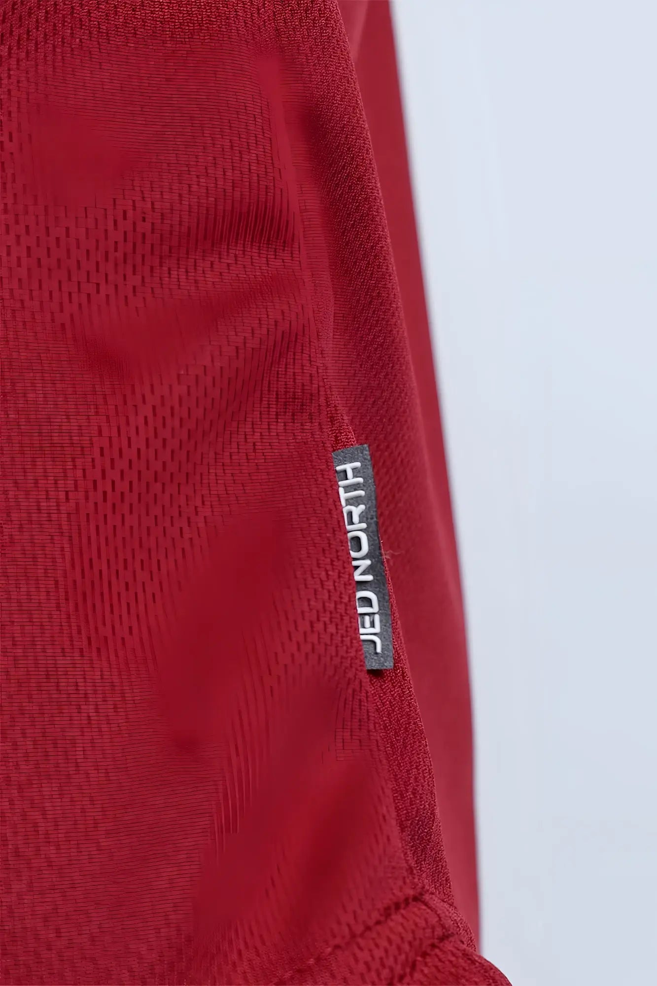 Maroon fast-dry bodybuilding workout stringer with red textured fabric and black jed north brand tag sewn in seam