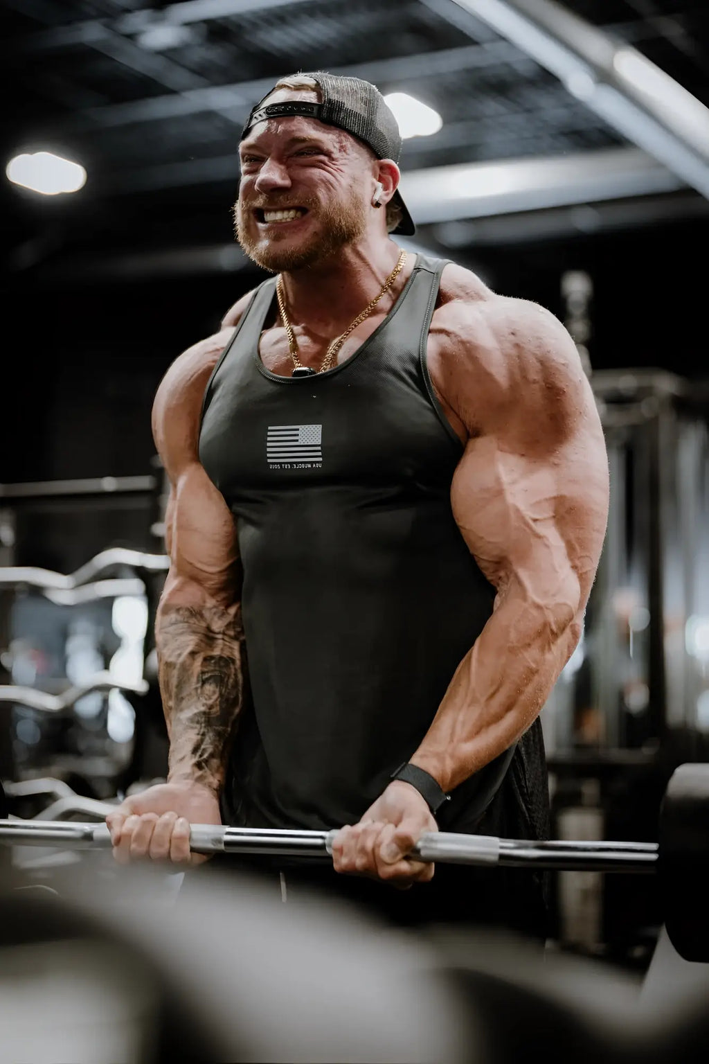 Muscular man wearing a black fast-dry bodybuilding workout stringer tank top with an american flag logo and gold chain necklace