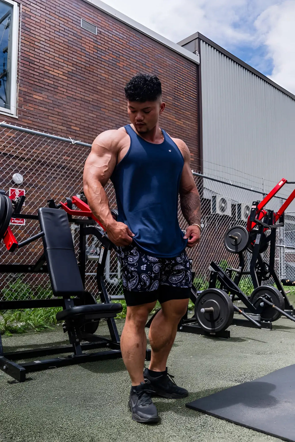 A muscular man wearing a navy jed north fast-dry bodybuilding workout stringer with black paisley shorts